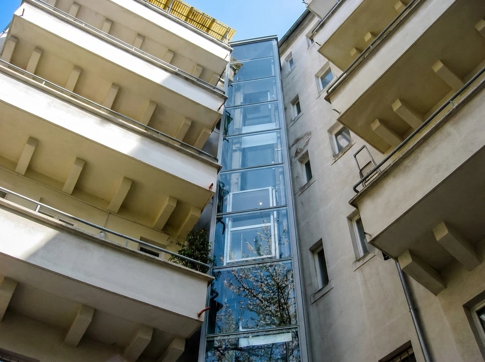 Deux ascenseurs modernes dans un hall d'immeuble contemporain, l'un ouvert révélant l'habitacle éclairé avec main courante et parois inox, l'autre fermé avec portes coulissantes métalliques